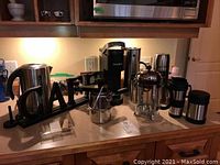 Countertop view showing Breville electric kettle, Keurig coffee maker, French press, multiple travel mugs, and a decorative 'LAKE' sign.