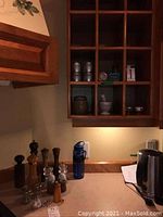 Wide view of kitchen corner with wooden shelves and multiple salt and pepper mills, glass shakers, and a blue water bottle on counter.