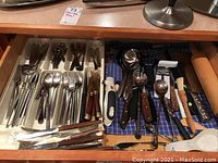 Overhead view of cutlery drawer showing forks, spoons, knives in white tray and other utensils on blue cloth