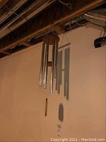 Front view of metal and wood wind chime hanging from ceiling with six metal tubes and wooden circular top and striker.