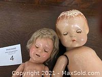 Close-up image of two 1930s dolls showing faces and upper bodies; one doll has molded hair, the other has a wig; both show wear and marks.