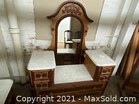 Antique vanity with three white marble tops and a tall attached mirror. Wood finish with ornate details and three sections including a central seat and side cabinets.