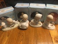 Photo showing four Precious Moments figurines with matching blue boxes behind, arranged on a wooden floor, depicting children and religious themes