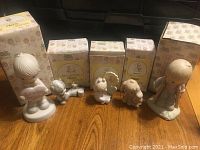 Photo showing multiple Precious Moments figurines alongside their original matching boxes, arranged on wood surface.