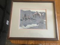 Framed print showing two cowboys sitting by a campfire with horses nearby, matted and framed in wood with bronze finish.