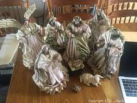 Photo showing the complete nativity set including Mary, Joseph, baby Jesus in a manger, three wise men, angel and two sheep figures all arranged on a wooden table.