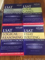 Four Kaplan LSAT test preparation books on reading comprehension, logic games, logical reasoning, and essay writing, each labeled with the respective strategy and tactics, 100% official LSAT questions, with bold colored headers.