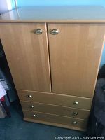 Upright cabinet with two doors on top and three drawers below. Birch finish, brass cup pull handles.