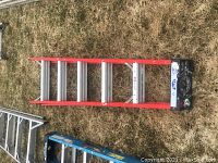 Top view of 6-foot red aluminum ladder lying on grass with five wide steps.
