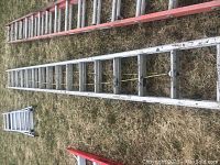 Two ladders laying on grass, one aluminum and one red fiberglass, showing overall condition and length