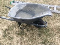 Photo of the gray plastic wheelbarrow showing the basin and metal frame on a grass surface, with visible dirt and wear marks.