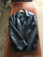 Front view of Danier black leather coat laid flat on wooden table, showing classic style and smooth leather texture