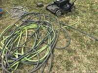 Black self-propelled lawnmower next to coiled garden hoses on grass