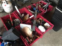 Overall view of seven red collapsible plastic containers filled with various hand tools, hardware items, and accessories such as clamps, levels, cables, and measuring tools.