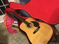 Photo showing the acoustic guitar inside a hard case with red interior lining, highlighting the overall condition and inclusion with case.