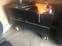 Full view of the large black metal job box with four caster wheels.