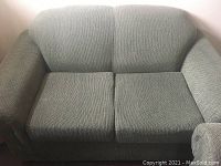 Green loveseat viewed from front showing cushioned seat and back, rounded arms, upholstered in textured green fabric