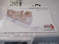 Box of the baby scale showing the branding and image of a baby on the scale
