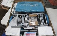 Boxed Pilates Pro Chair components including steel frame parts, pedals, sculpting handles, and blue padded seat upholstery.