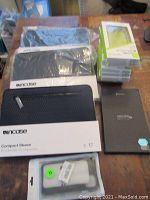 Multiple new tablet and phone cases including Incase Compact Sleeves and Urban Armor Gear phone cases in original packaging on wooden table.