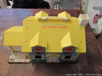 Top view of Fisher Price Play Family House showing yellow roof with two dormer windows and chimney, branding visible on roof surface.