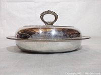 Side view of the silver-tone oval serving dish with lid, showing thickness and subtle tarnish.