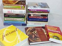 Stack of various cook books including titles about sausage making, Japanese cuisine, desserts, and French cooking.