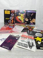 Photo of the full lot of 16 sheet music books with covers visible showing a variety of music types and instruments.