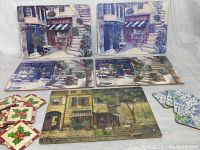 Photo of five rectangular placemats laid out with vintage European street scene prints showing storefronts, stairs, and windows in muted tones.