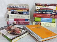 Cookbooks arranged in two piles showing 'Bread Alone,' 'The Duck Cookbook,' 'Charcuterie,' and other titles with visible wear and tear.