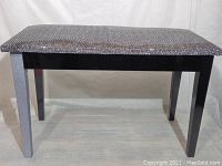 Front and side view of the piano bench showing black finish with silver textured front legs and snakeskin-like patterned cushioned seat.