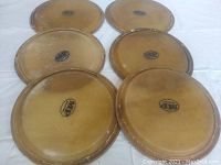 Six natural tan bongo heads arranged on a white surface, showing their shape, wear and rust on rims.