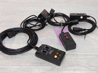 Four fog machine remote controls with attached cables, various button and switch configurations.