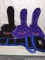 Front view of three guitar soft cases, two purple Gypsy Rose and one black Gypsy Rose, plus one black and blue NBA case laid out flat against plain white background.