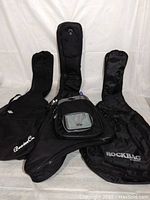 Three black guitar soft cases of different sizes laid out, showing front pocket, logos and general condition