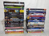 Photo showing stacked DVDs in two columns with titles visible, includes a mix of movies and concert DVDs.