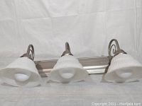 Full length view of the 3-light vanity light fixture showing metal backplate, curved arms, and frosted glass shades facing downwards.