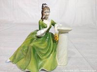 Front view of Royal Doulton Secret Thoughts figurine in green dress sitting by pedestal.