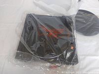 Turntable in plastic storage wrap, with visible circular turntable platter beneath black cover