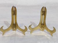 Pair of solid brass folding easels displayed upright showing double hinged design and polished brass finish.