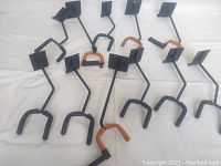 Eleven black metal guitar wall mount hangers with padded hooks laid on a white surface.