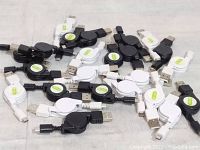 Top view of assorted black and white USB chargers with retractable cords piled together, showing variety and quantity.