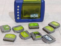Front view of the blue Mattel Juice Box media player and 9 media cartridges arranged in front