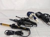 Five mixed hair styling tools: 3 curling irons and 2 blow dryers arranged on white surface, cords visibly wrapped.