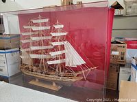 Wooden tall ship model schooner with multiple sails and masts inside a clear protective display case, shown from front and side angles.