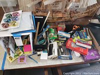 Overview of the lot showing scattered office supplies including tape dispensers, scissors, sticky notes, calculator, and pens on a table.