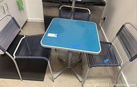 Blue square table with three matching metal chairs in a room with linoleum floor.