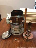 Disassembled parts laid out: refinery cap, glass lens, side bracket, fuel tank, wick assembly, main lantern body