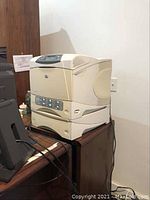 Full view of HP LaserJet 4200TN printer with attached accessory sitting on a wooden desk, beige color.