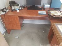 Front view of L-shaped wooden office desk with attached two-drawer cabinet, showing workspace with phone, monitor, and mousepad.